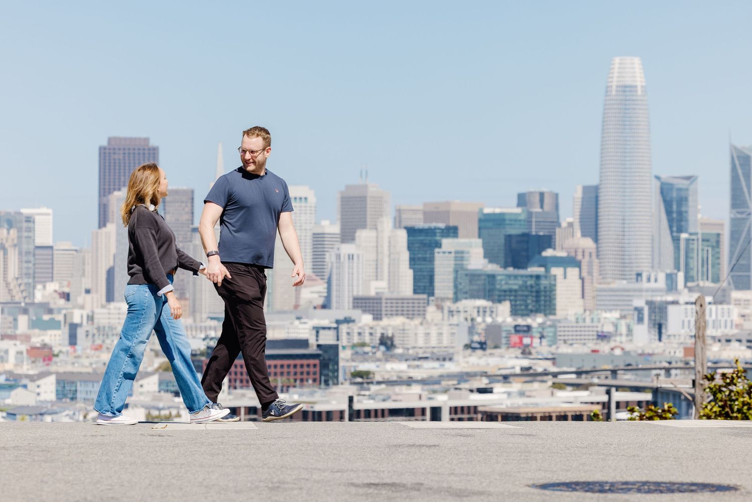 Couple walking hand in hand on a rooftop with the San Francisco city skyline in the background.