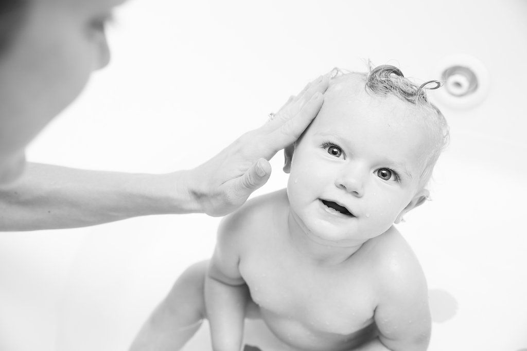 Black and white photo of a baby getting hair washed by an adult hand during bath time.