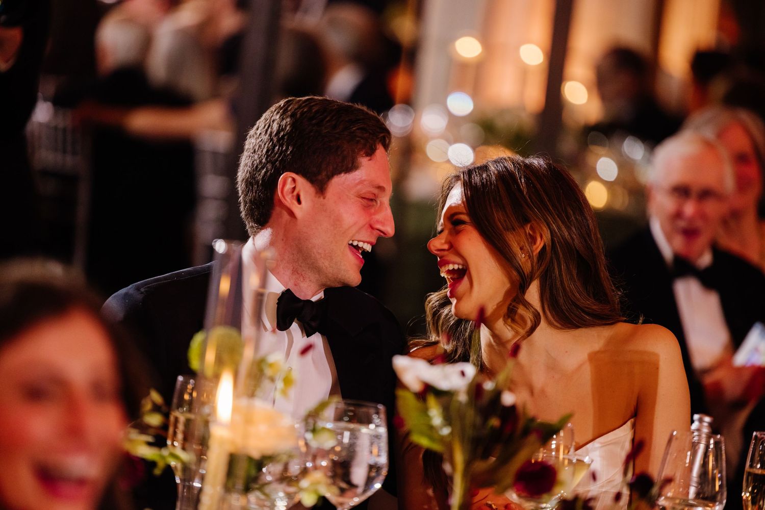 Bride and groom sharing joyful laughter at elegant candlelit wedding reception dinner.