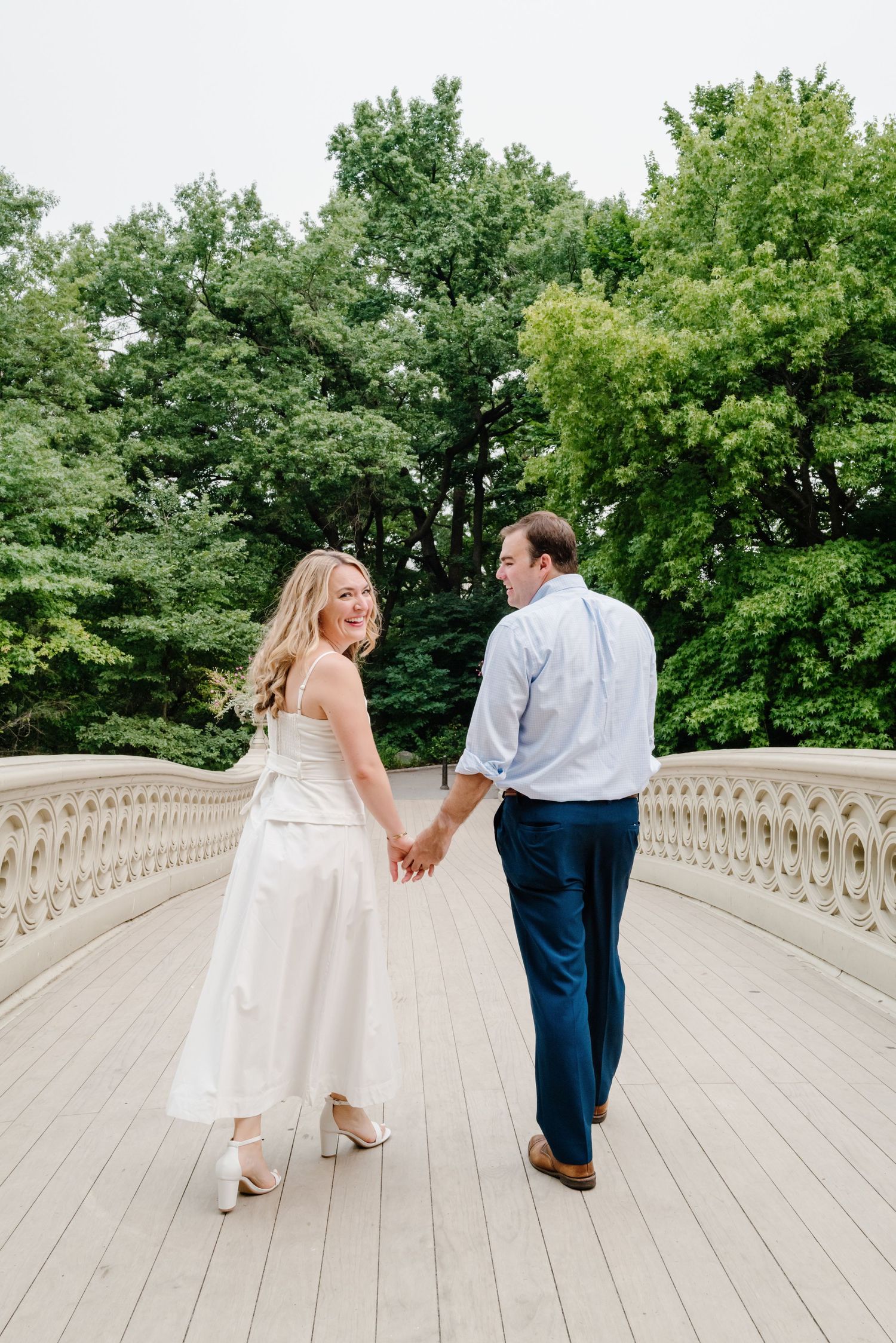 Bride and groom holding hands walking on Bow Bridge in Central Park, NYC.