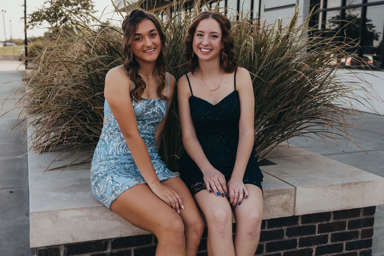 Two young people in summer dresses sit together on a brick ledge outdoors.