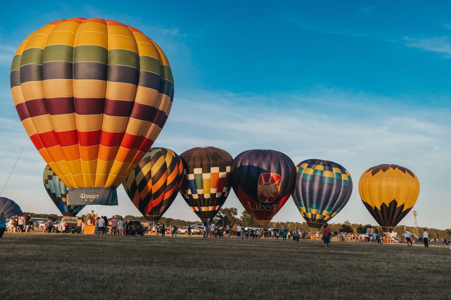 Row of colorful hot air balloons lined up on ground during morning festival.