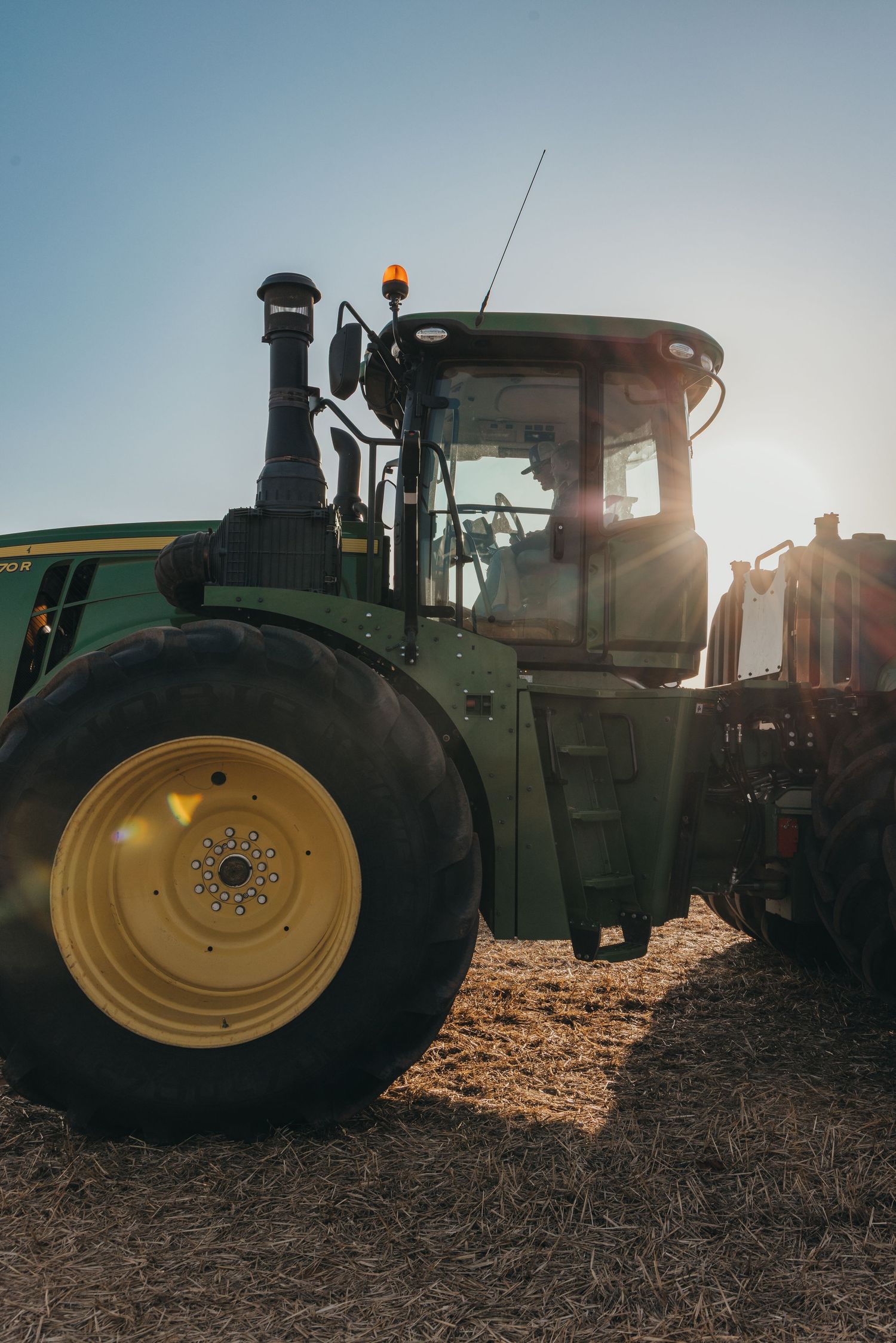 Silhouetted tractor tires against a backlit sky create a dramatic agricultural scene during golden hour lighting.