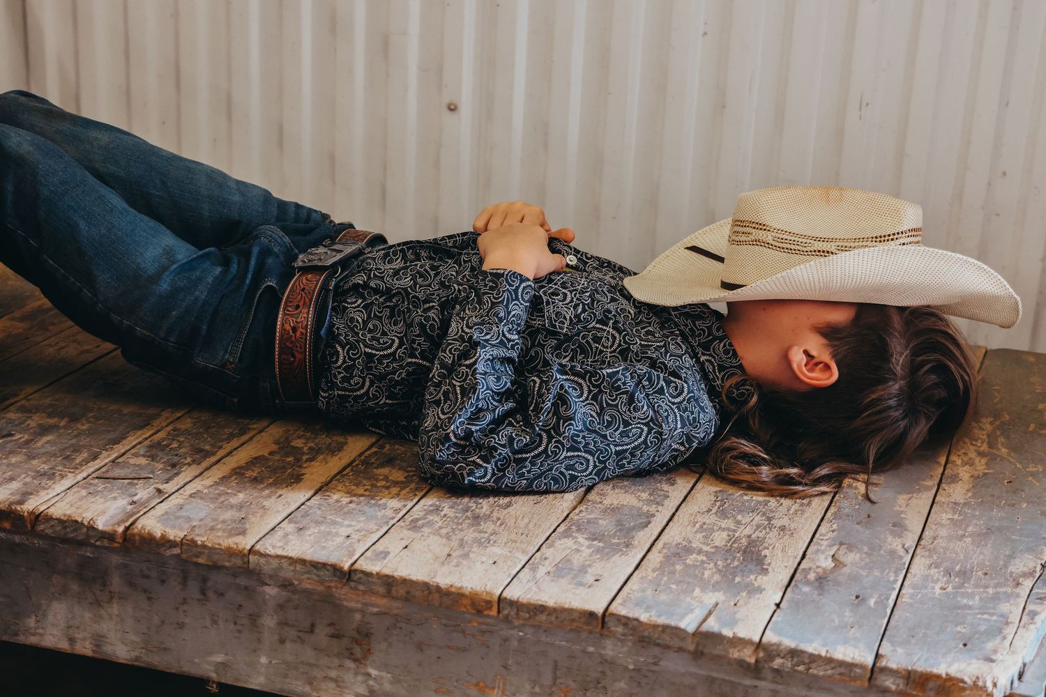 Person resting on wooden platform wearing cowboy hat and jeans.