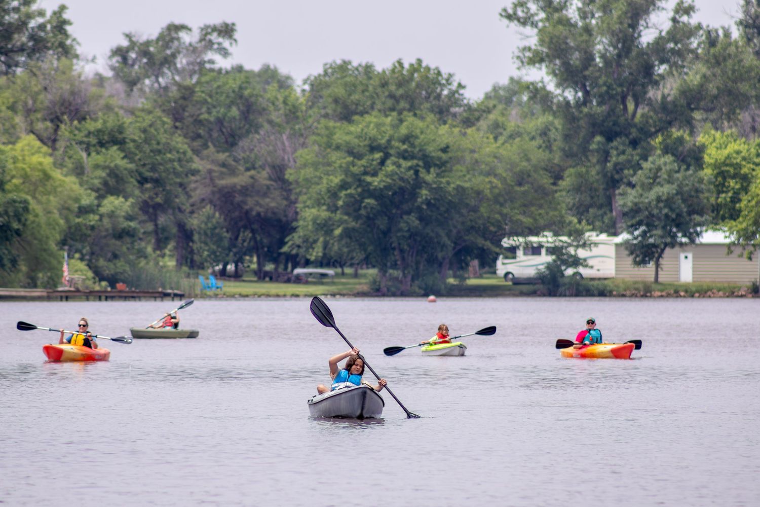Multiple kayakers enjoy a day on the lake with colorful boats dotting the water.