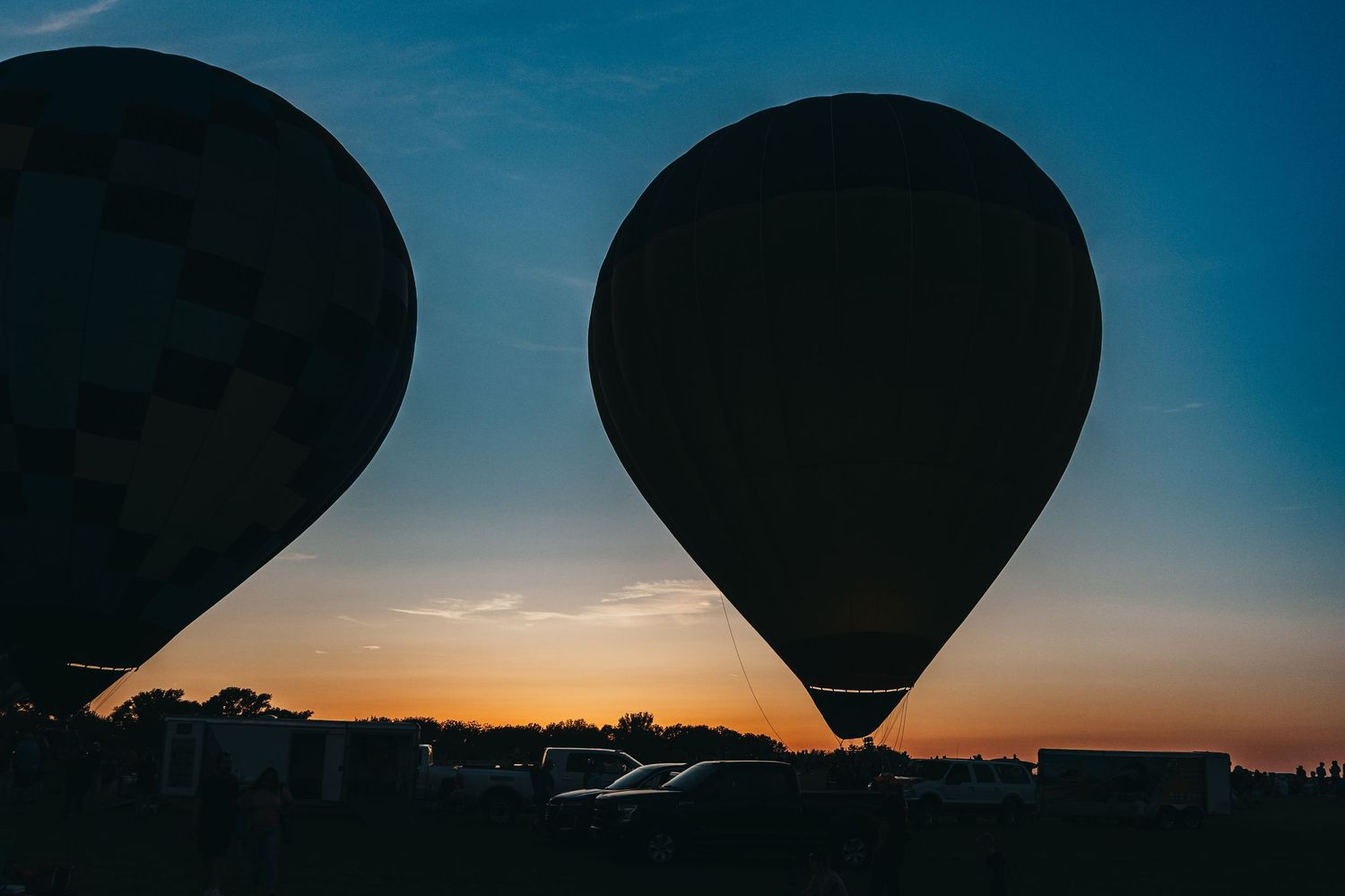Two hot air balloons silhouetted against a sunset sky during a festival.