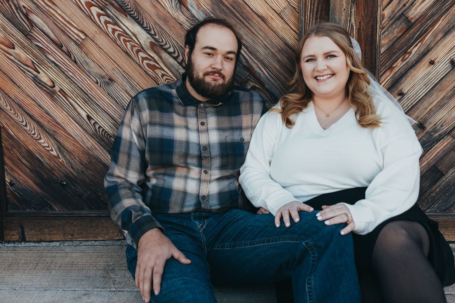 A couple poses together against a rustic wooden wall background in a series of candid engagement photos.