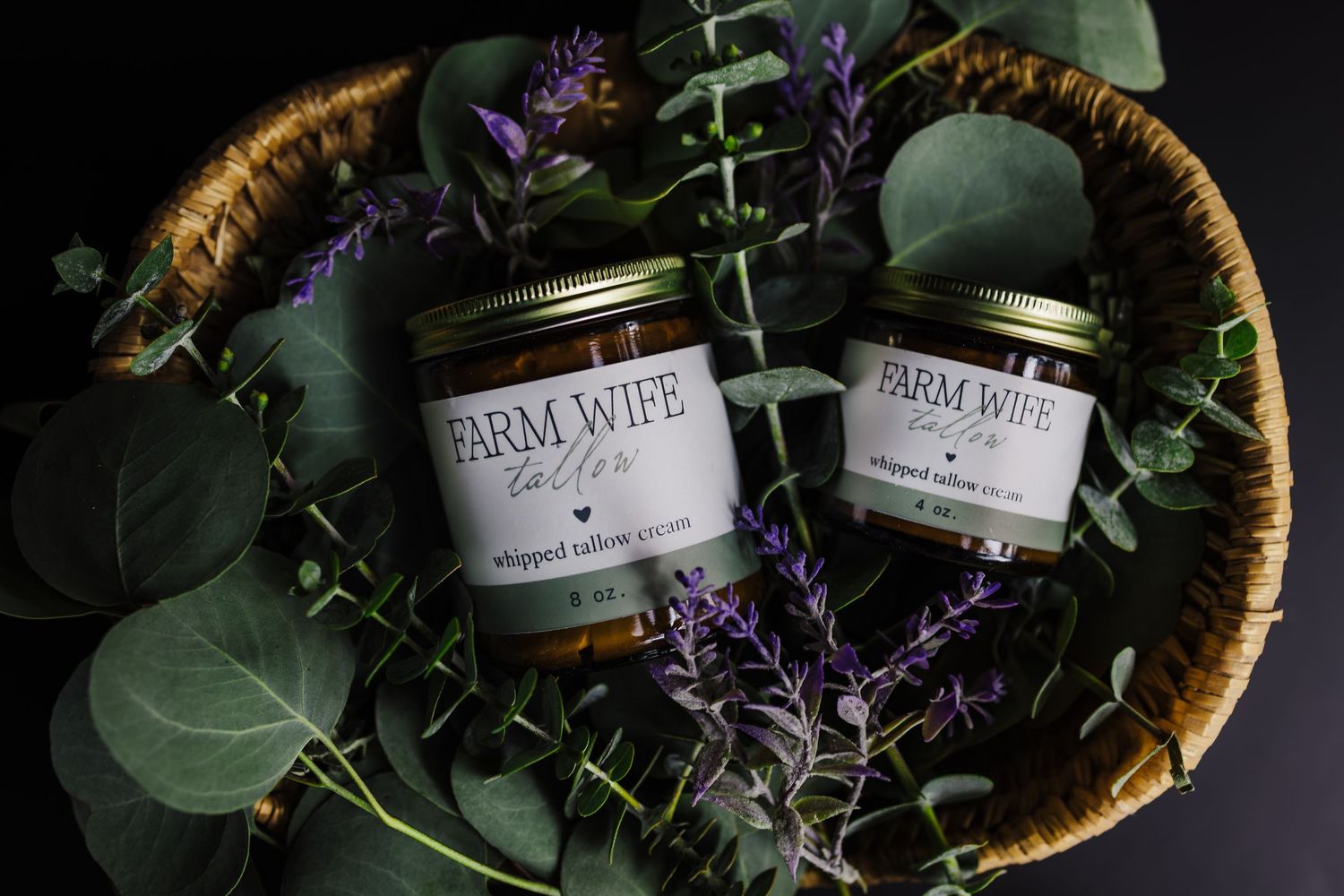 Rustic woven basket filled with artisanal honey jars and fresh purple florals against a dark background.