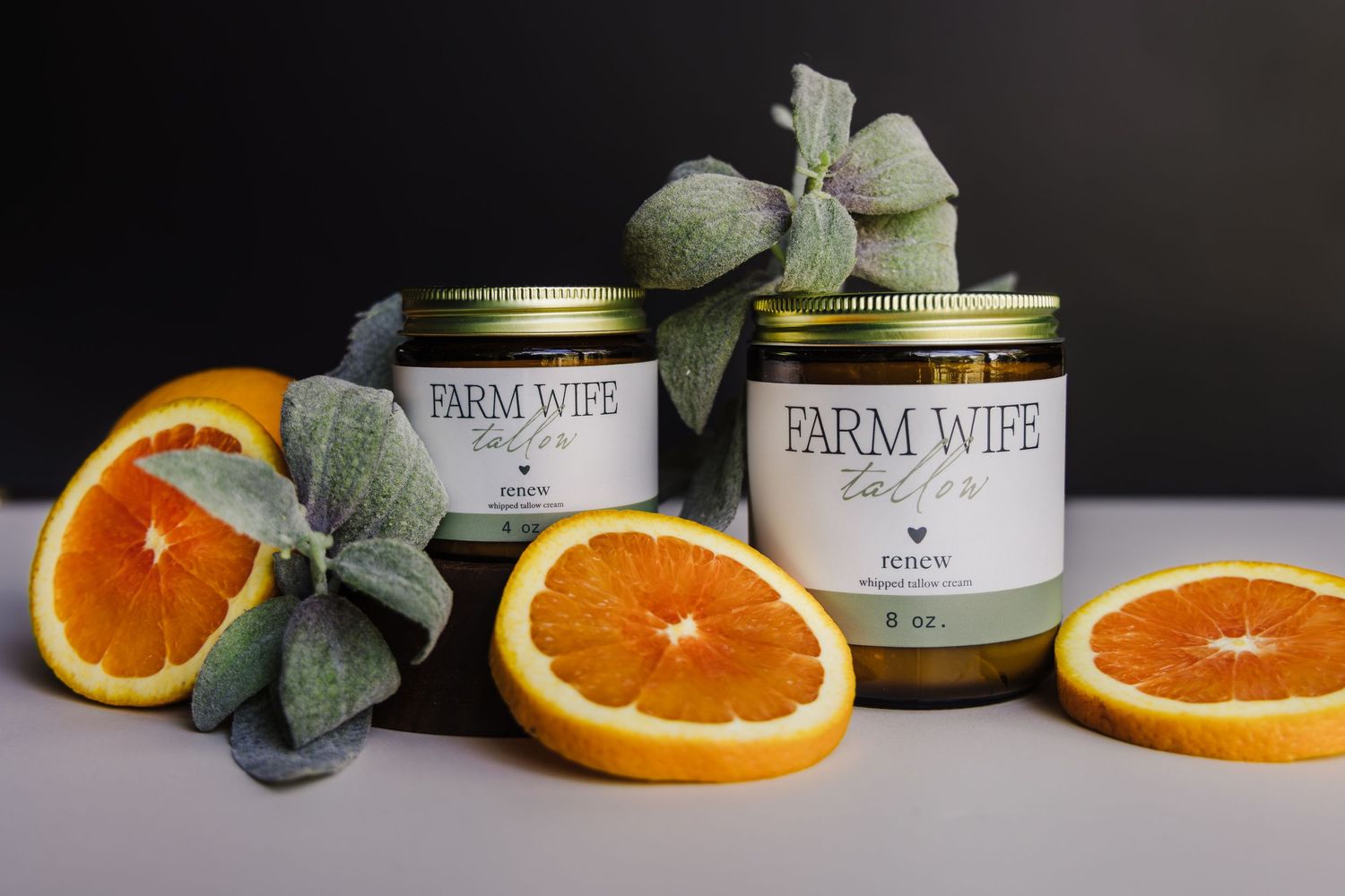 Fresh orange slices and eucalyptus leaves arranged with Farm Wife branded jars on a light surface.