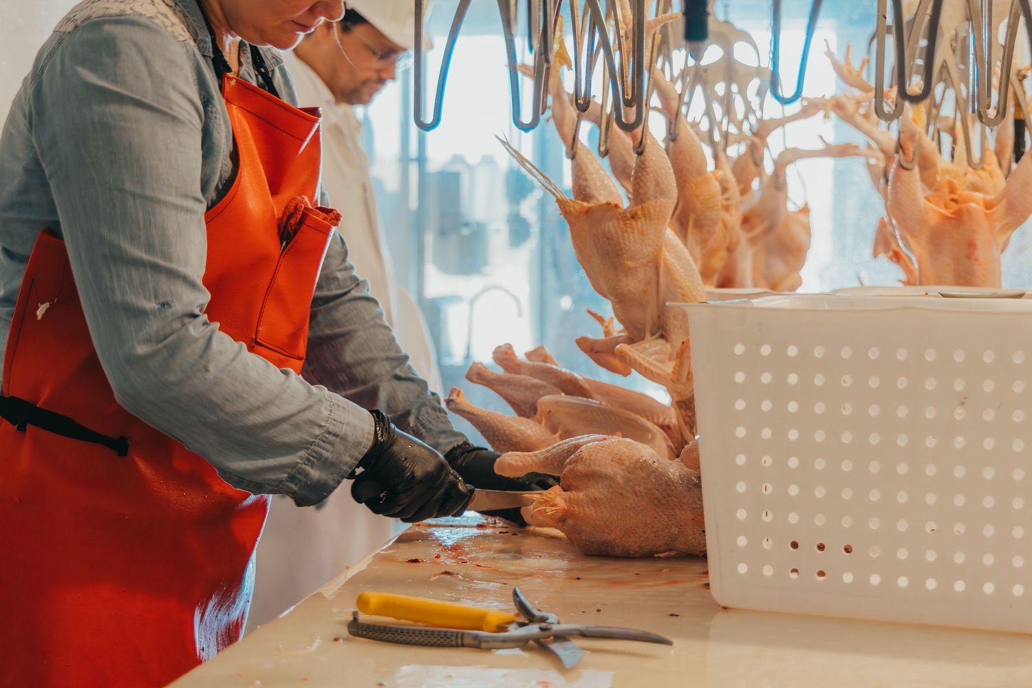 Worker in red apron processing poultry on a commercial cutting board.