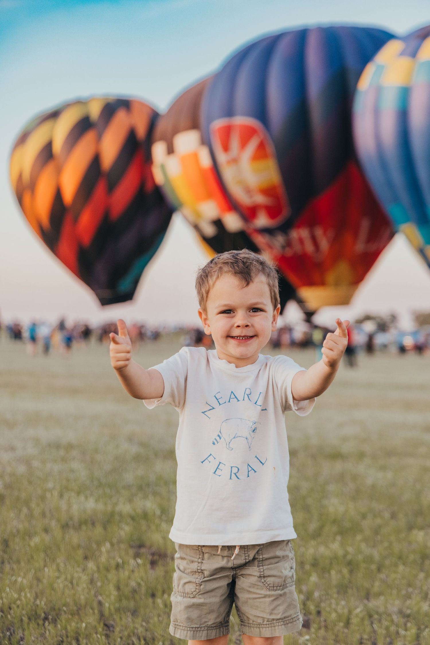 Colorful hot air balloons lined up at a festival with spectators in the foreground.