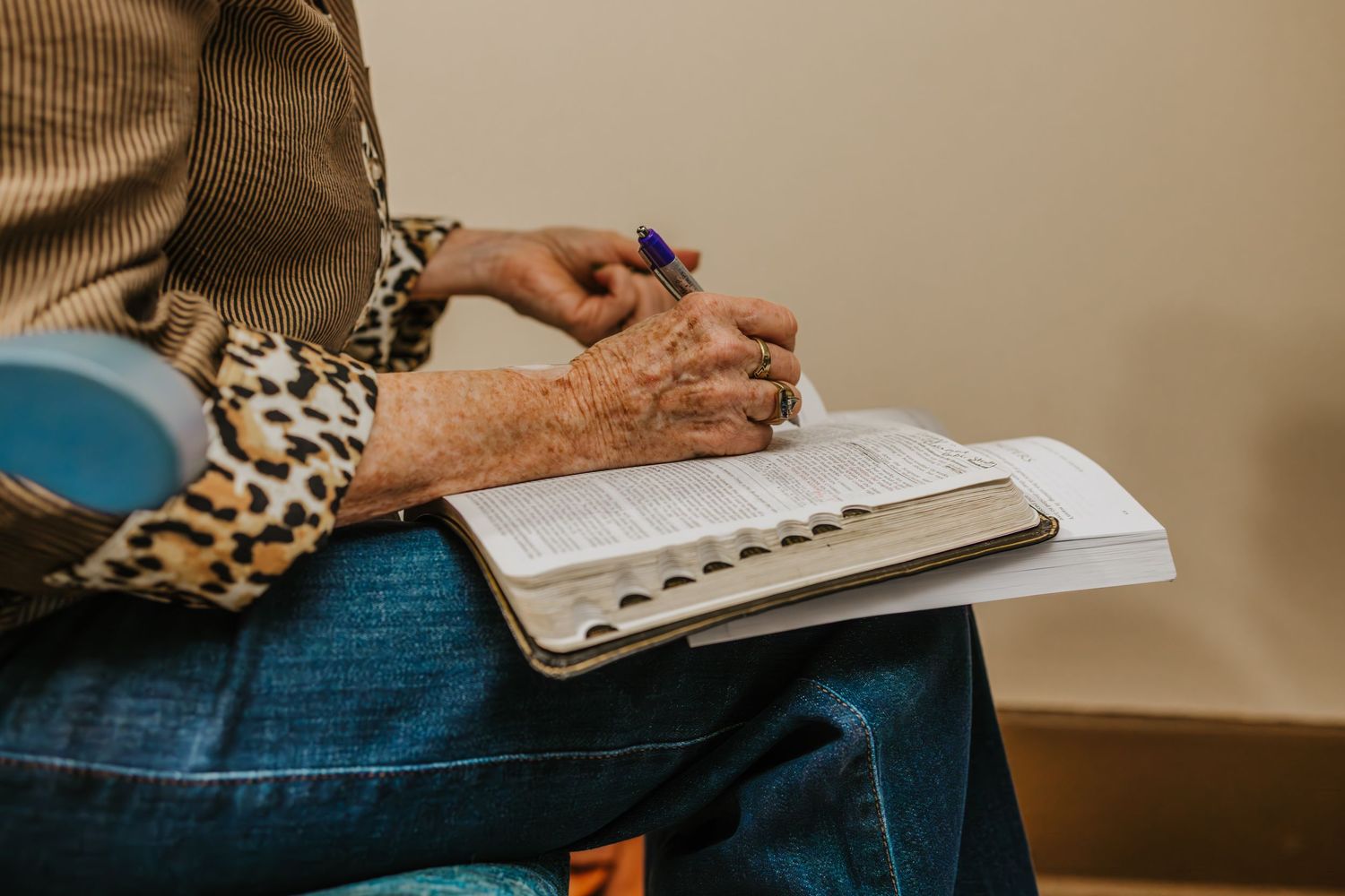 Person wearing jeans and animal print sits with an open notebook on their lap while writing with a pen.