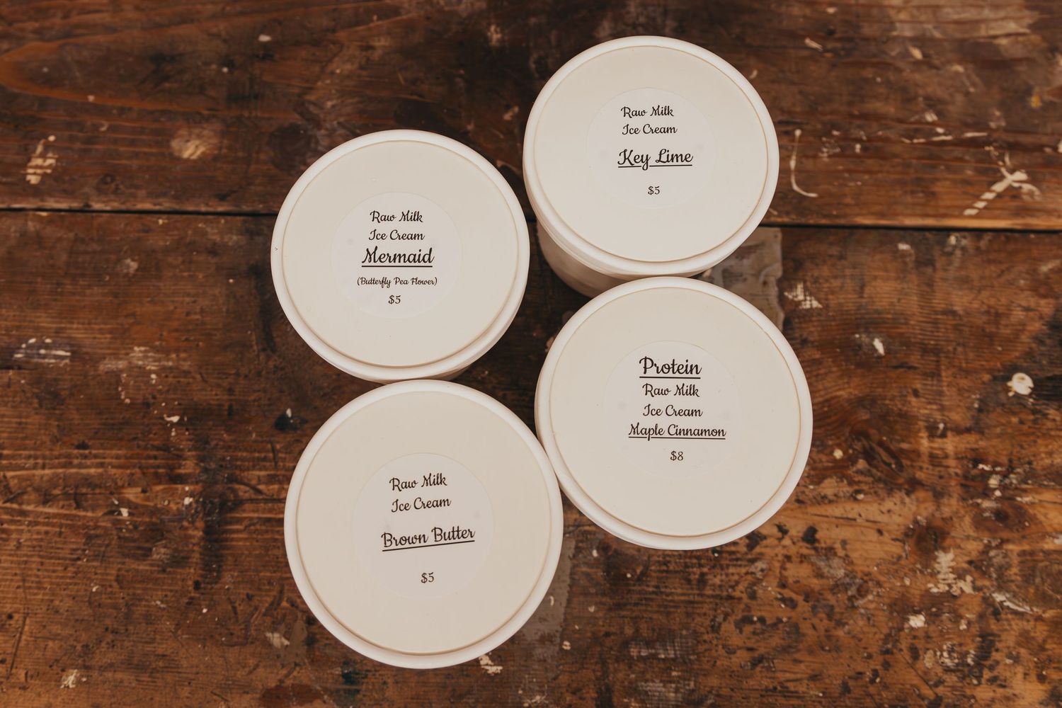 Four white circular candle lids with text arranged on dark wooden surface.