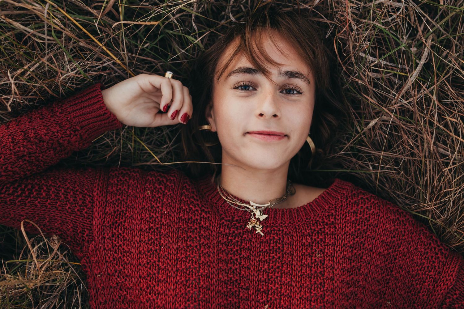 Person wearing a red sweater lies in autumn foliage creating a cozy seasonal portrait.