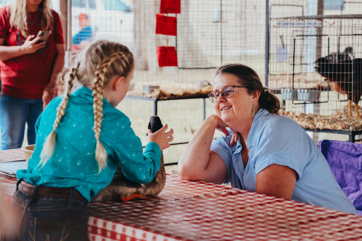 Two people engage in conversation at a red picnic table at what appears to be a fair or outdoor event.