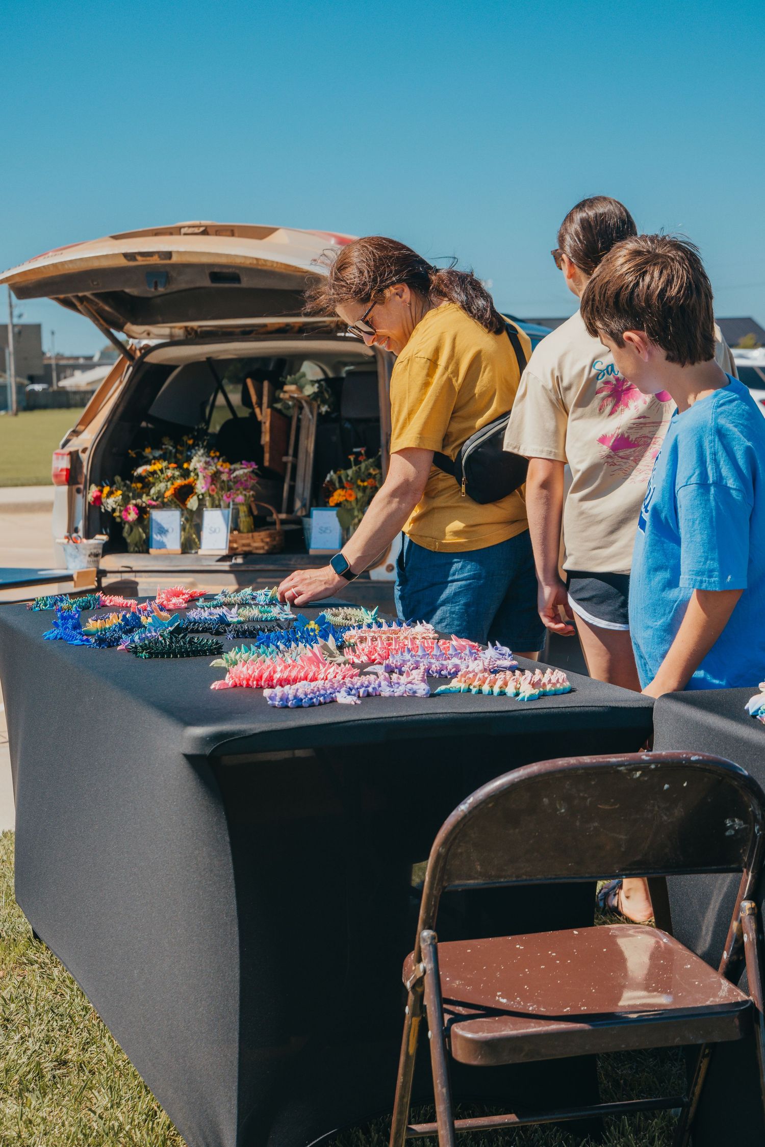 People gathered at outdoor tables sorting through colorful materials and supplies under a bright blue sky.