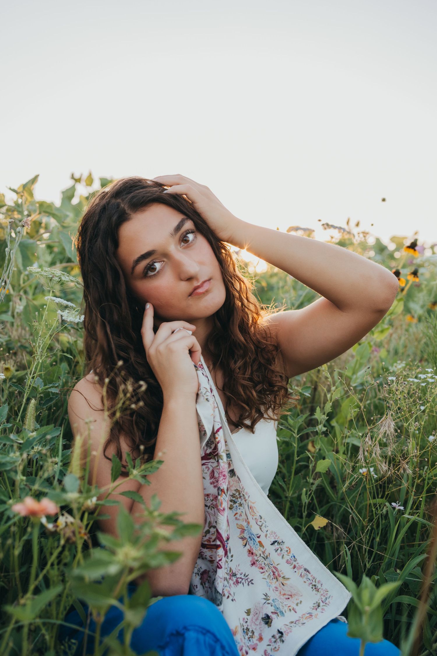 A dreamy portrait in a wildflower meadow shows a young woman in a floral top posing among blooming summer flowers.