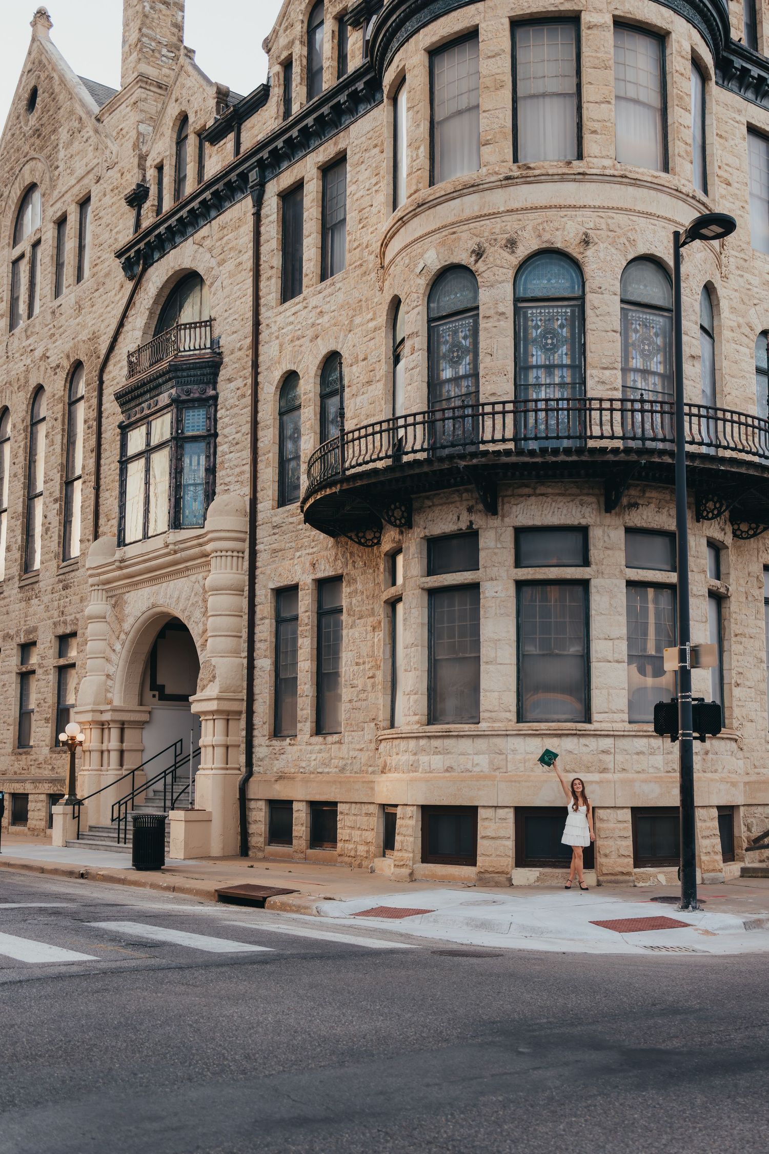 Woman in white dress standing beside a grand historic limestone building with ornate balconies at a street corner.