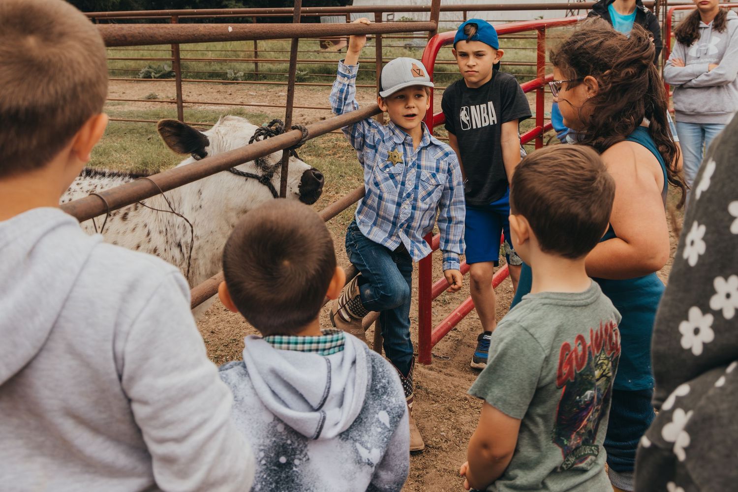 Small group of people gathered around a pen or enclosure at a farm or agricultural setting while someone appears to be teaching.
