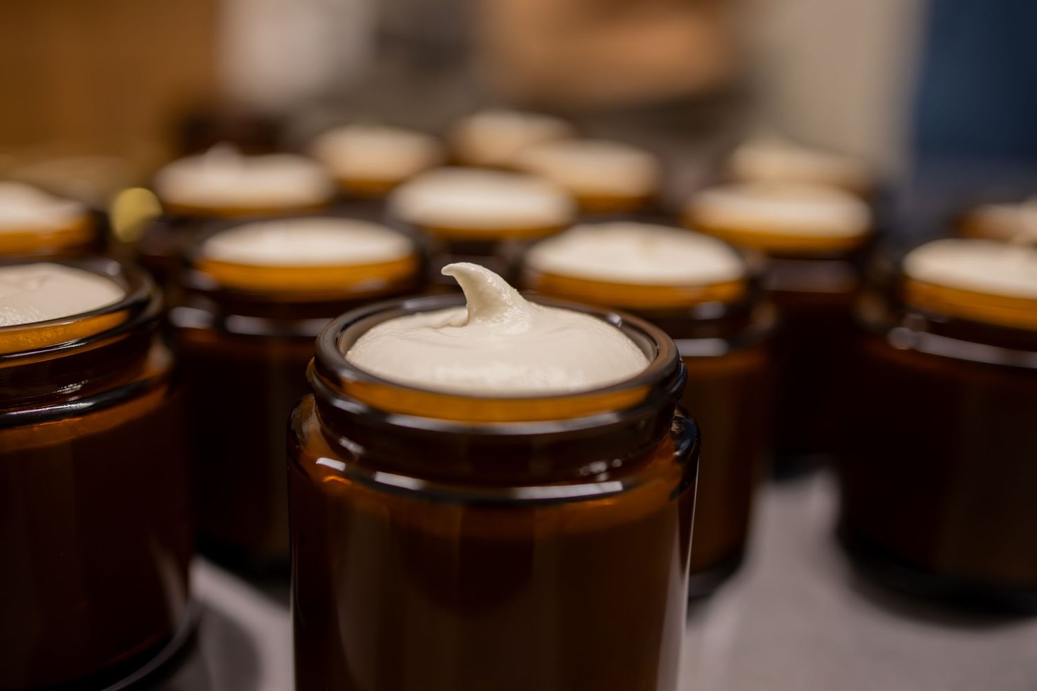 Several amber glass jars with white cream on top arranged in rows showing spa or skincare products.