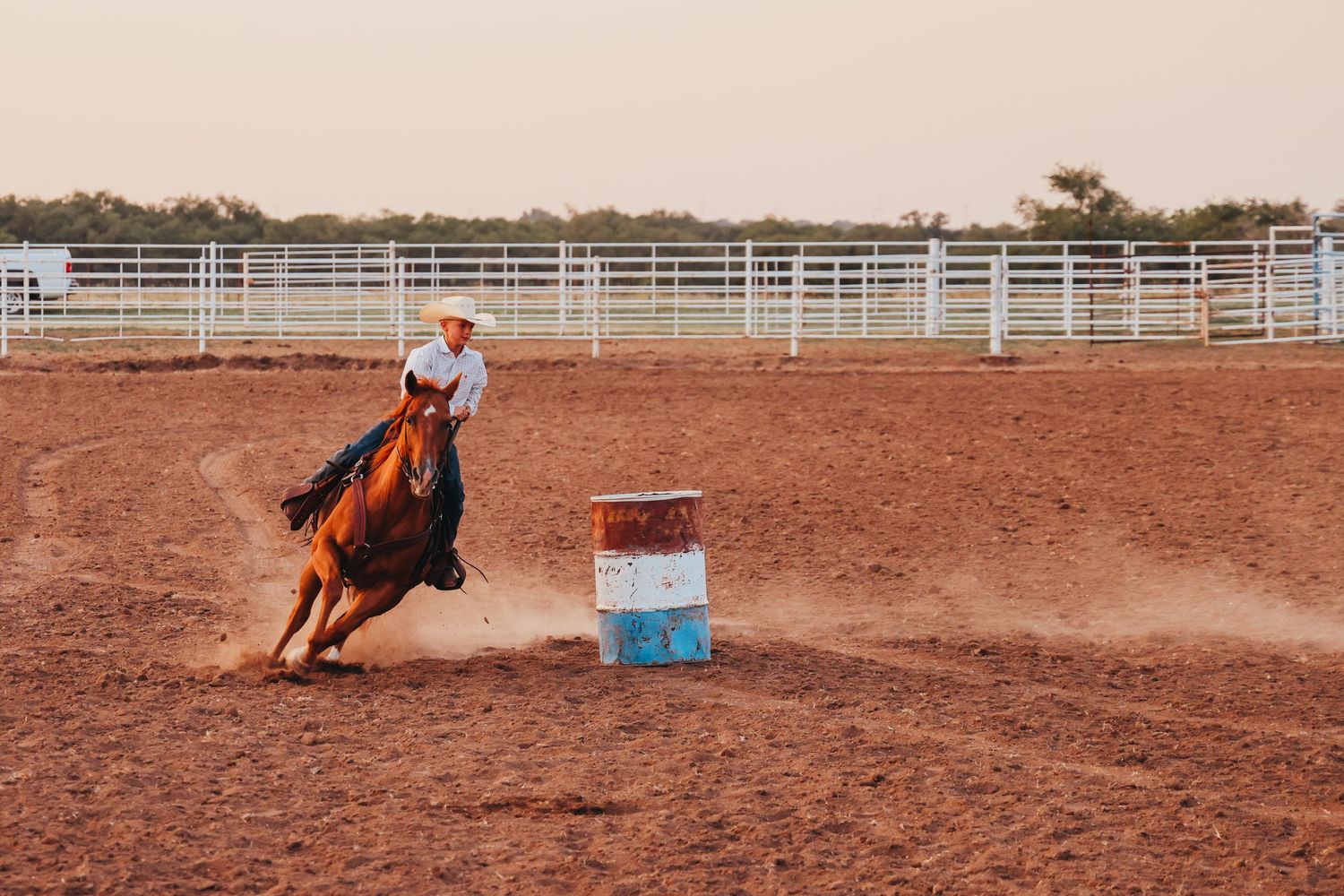 Horse and rider racing around barrel in dusty rodeo arena.