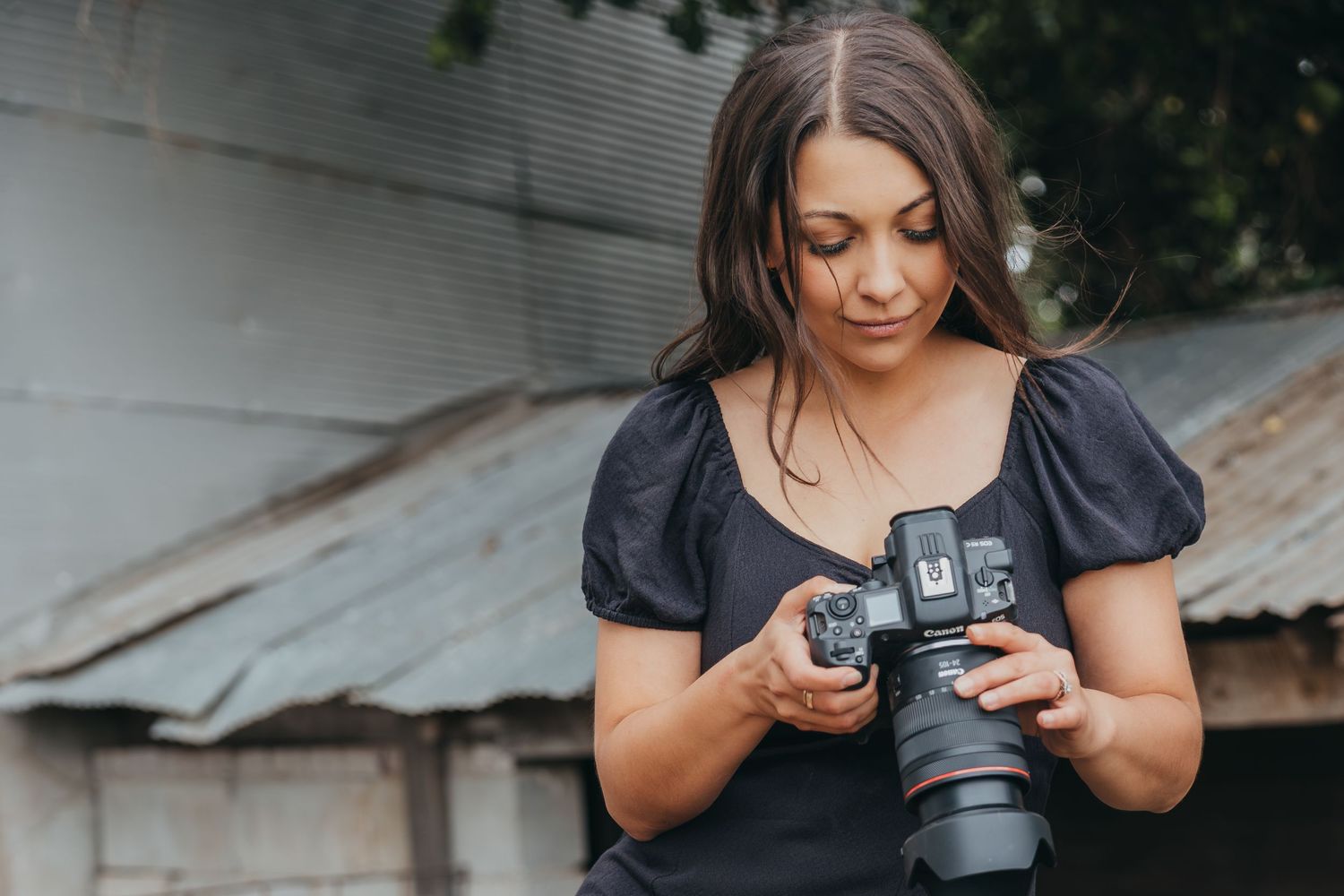 Photographer in black puff sleeve shirt reviews photos on camera display screen outdoors.
