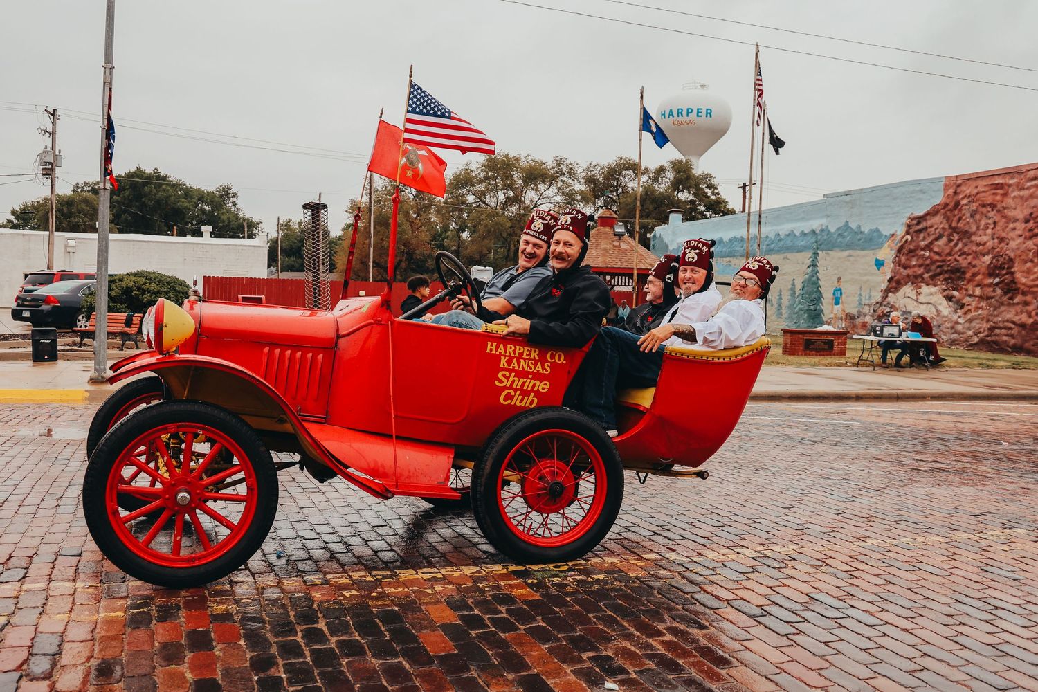 Red vintage Model T Ford decorated with American flags on brick street during parade.