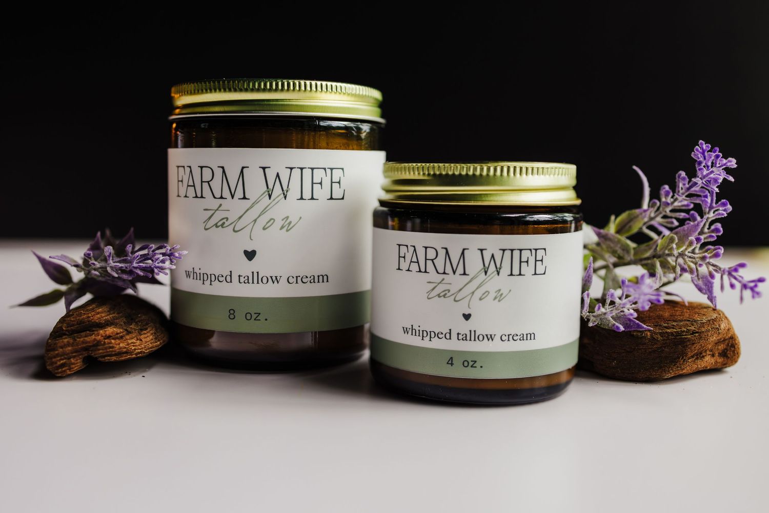 Mason jars with Farm Wife branding sit next to purple flowers and rustic decor on a wooden surface.