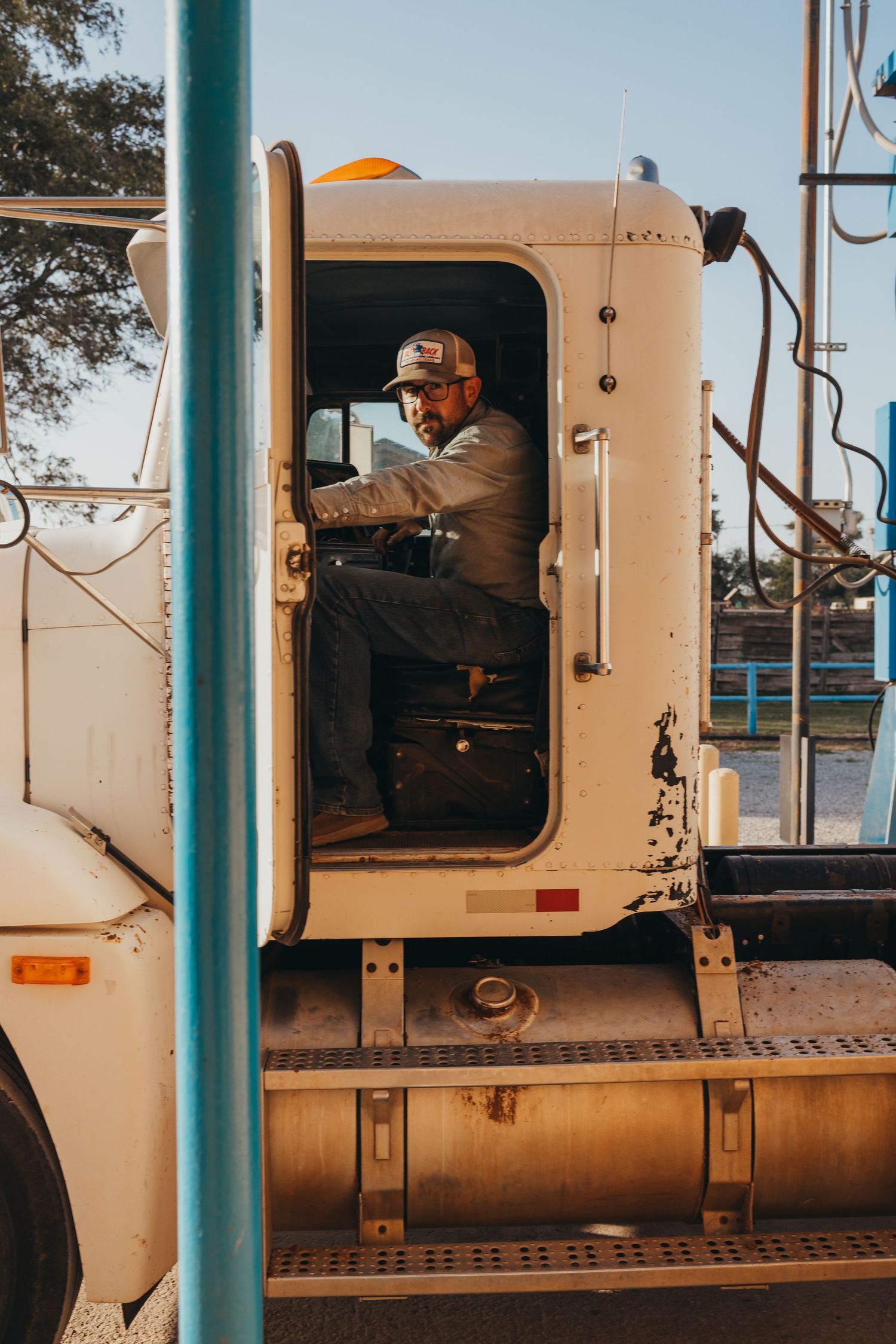 Side view of someone driving a large commercial truck cab in warm lighting on a sunny day.
