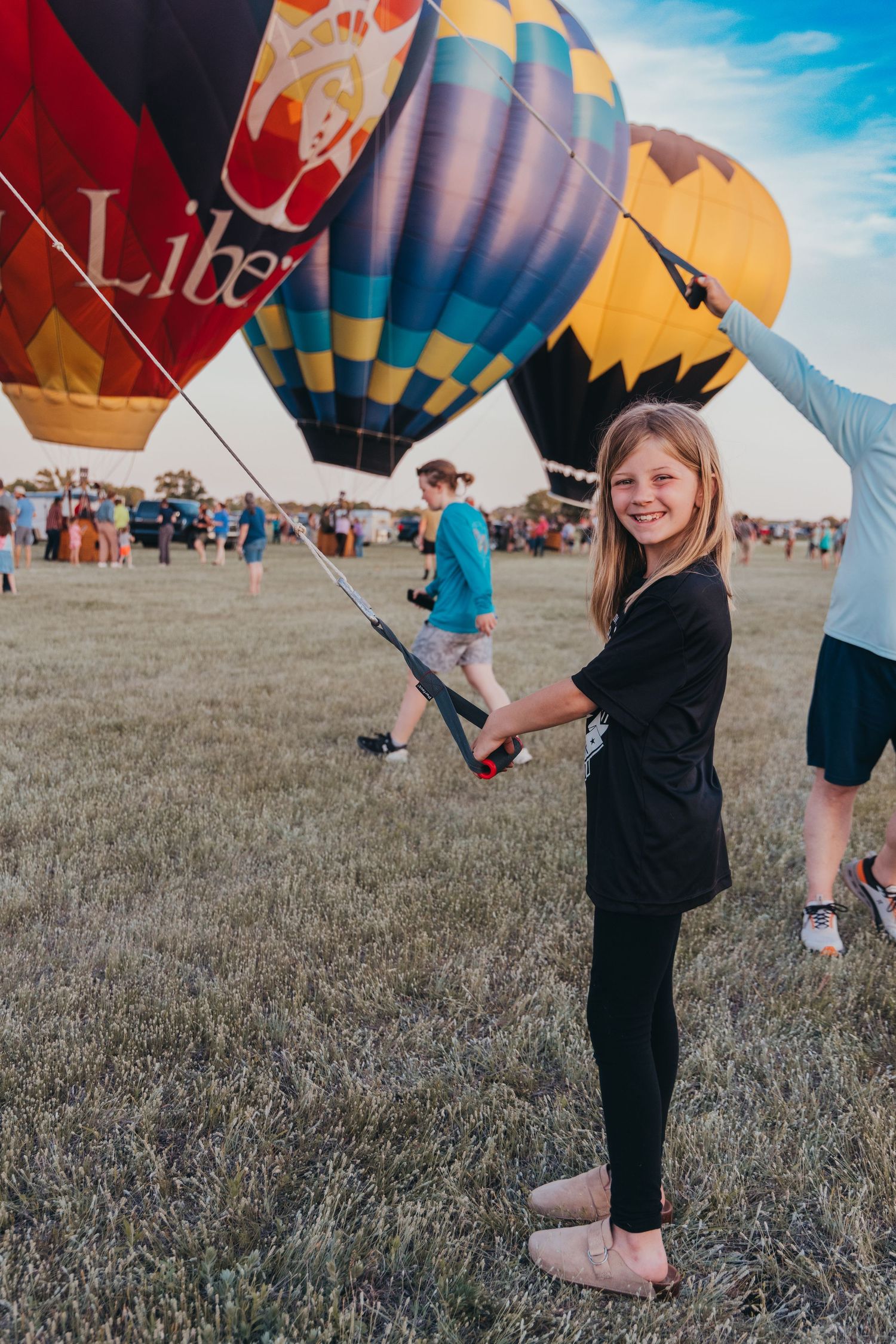 Colorful hot air balloons lined up at festival with spectator in foreground.