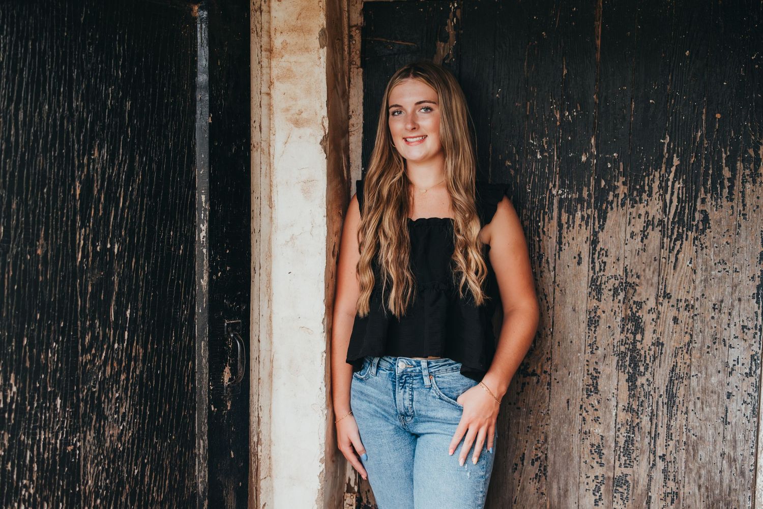 Fashion model posing against weathered wooden wall in casual denim outfit and brown top.