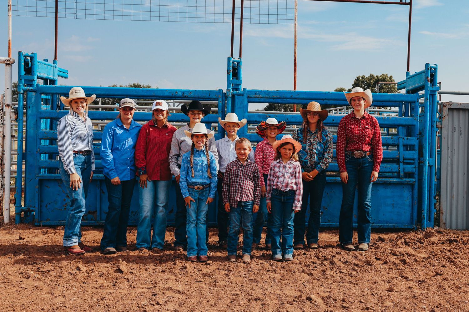A group poses in front of blue metal gates at a livestock event.