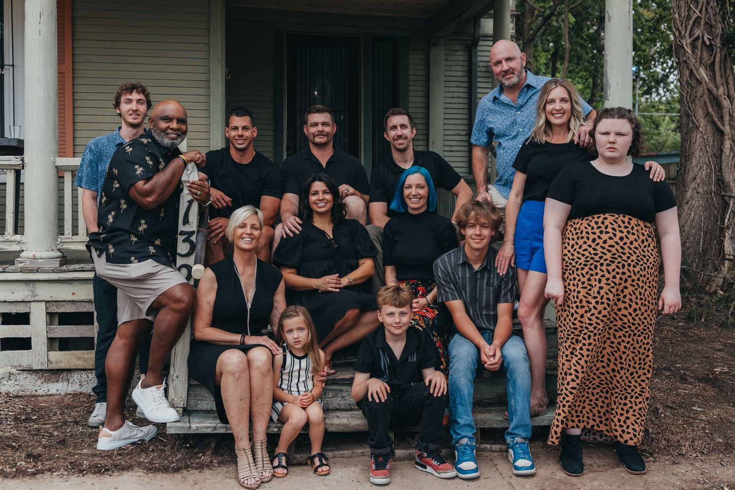 A large group poses together outdoors on a rustic porch wearing casual attire.