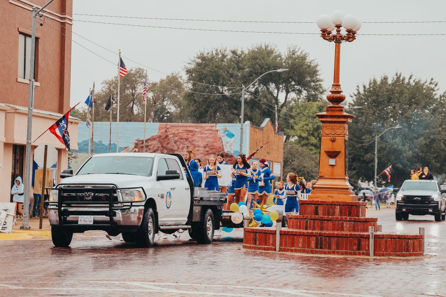 Pickup truck parked near decorative lamp post on wet street during small town parade.