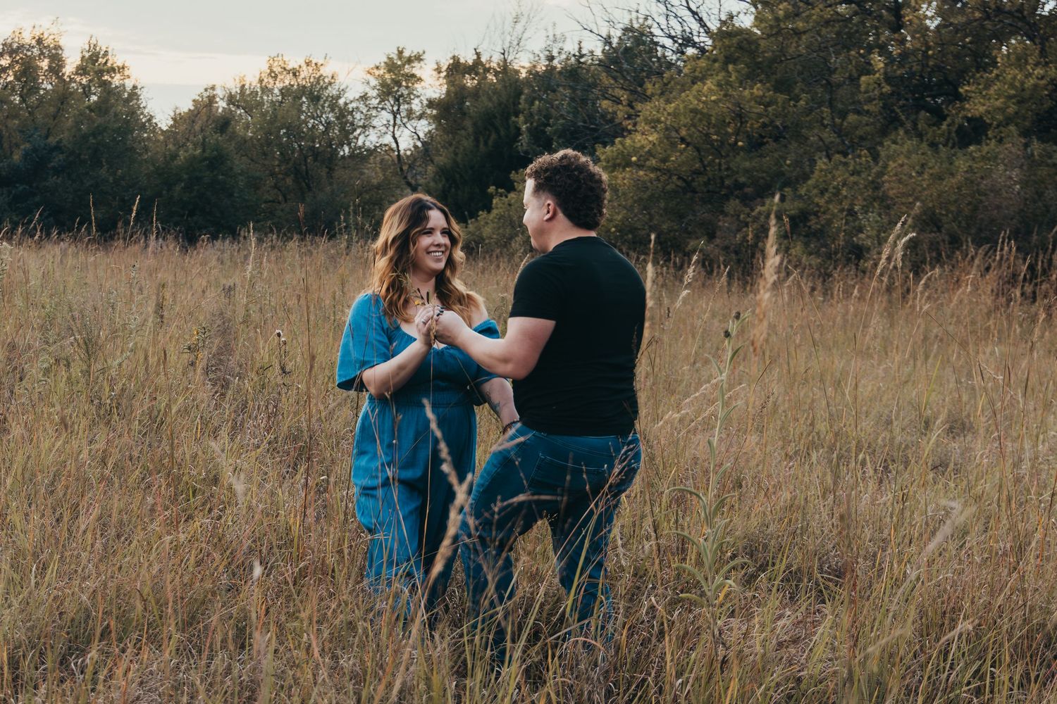 Couple embraces in a golden autumn field during sunset while wearing casual attire.