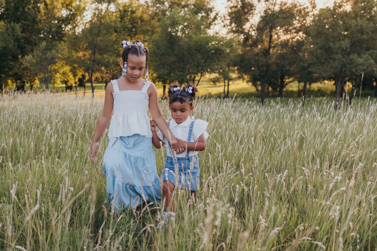 A family walks together through a sunlit meadow of tall grass during golden hour.