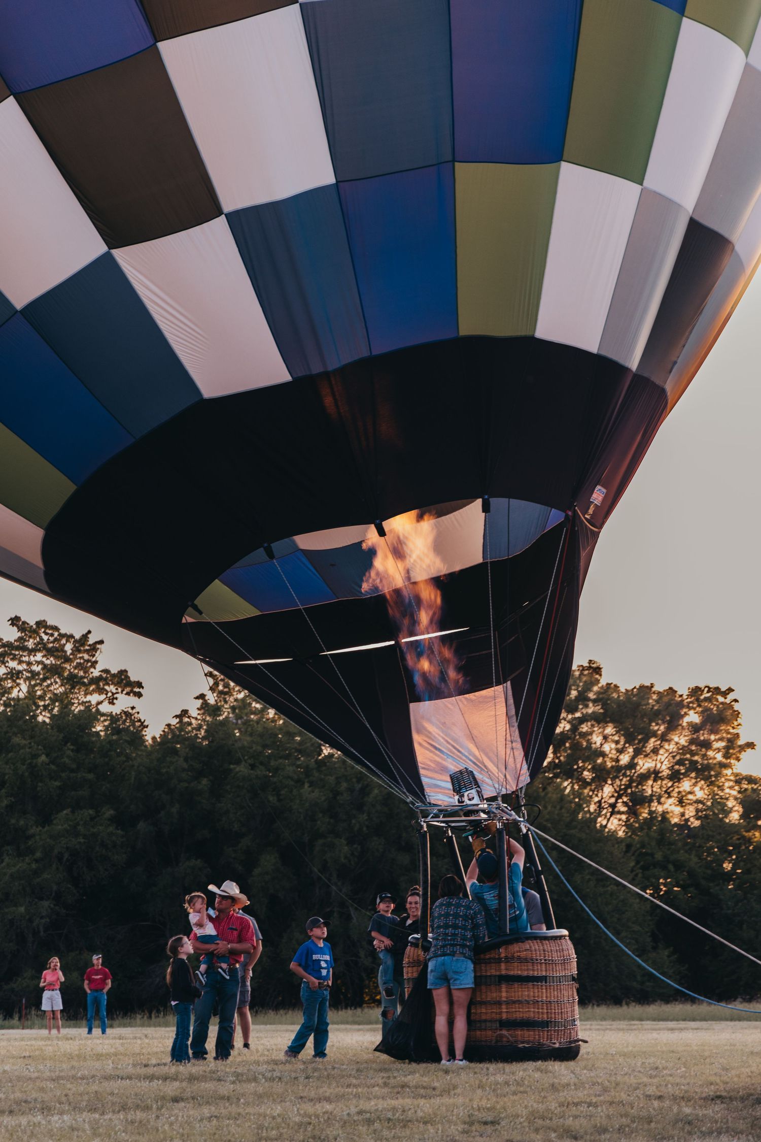 Hot air balloon burner firing up under a geometric patterned balloon envelope at dusk.