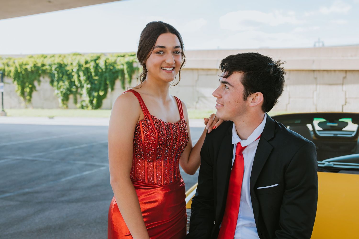 A couple smiles at each other, with her in a red sequined dress and him in a black suit with red tie.