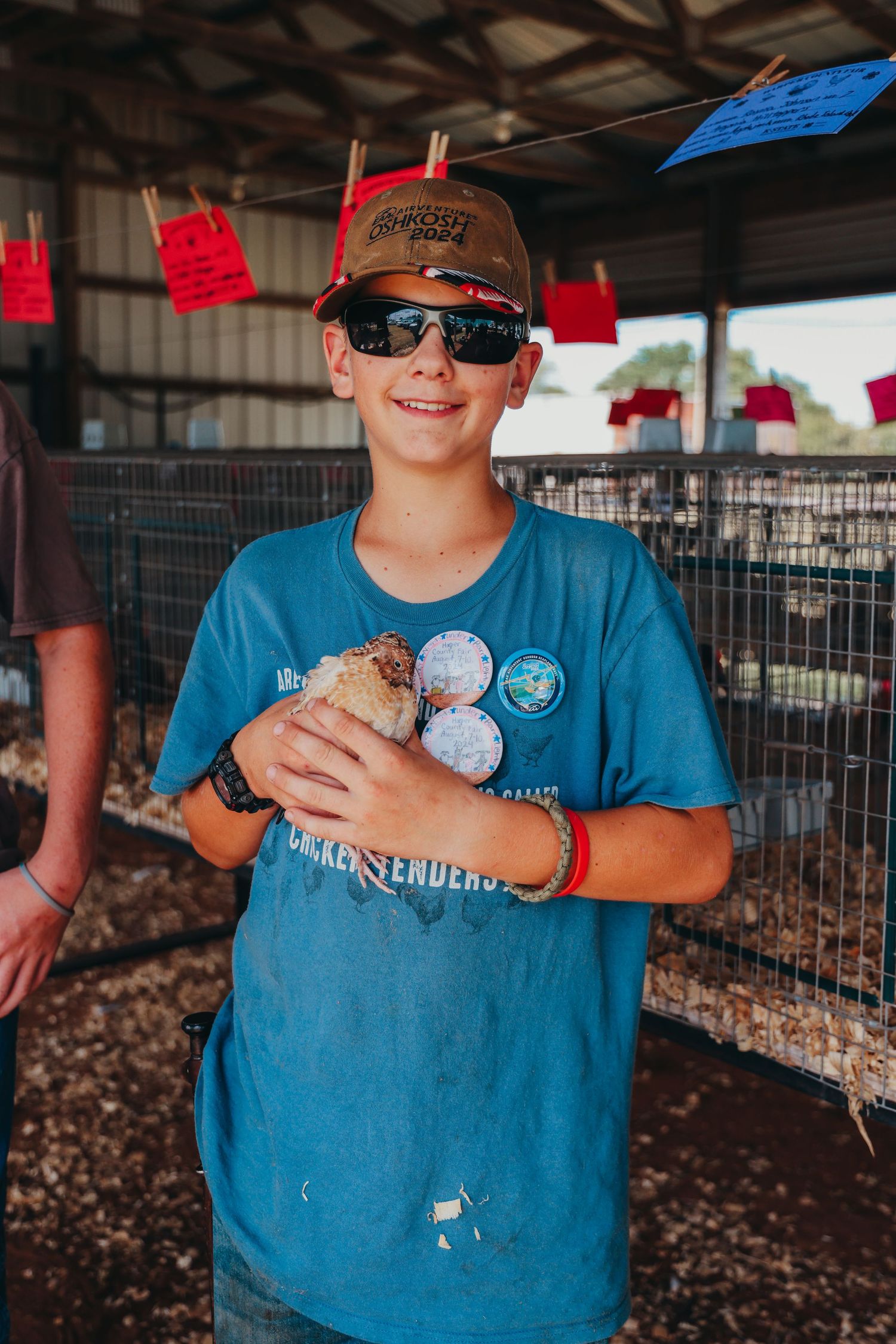 Youth holding baseball at a rural fair wearing blue t-shirt and cap.