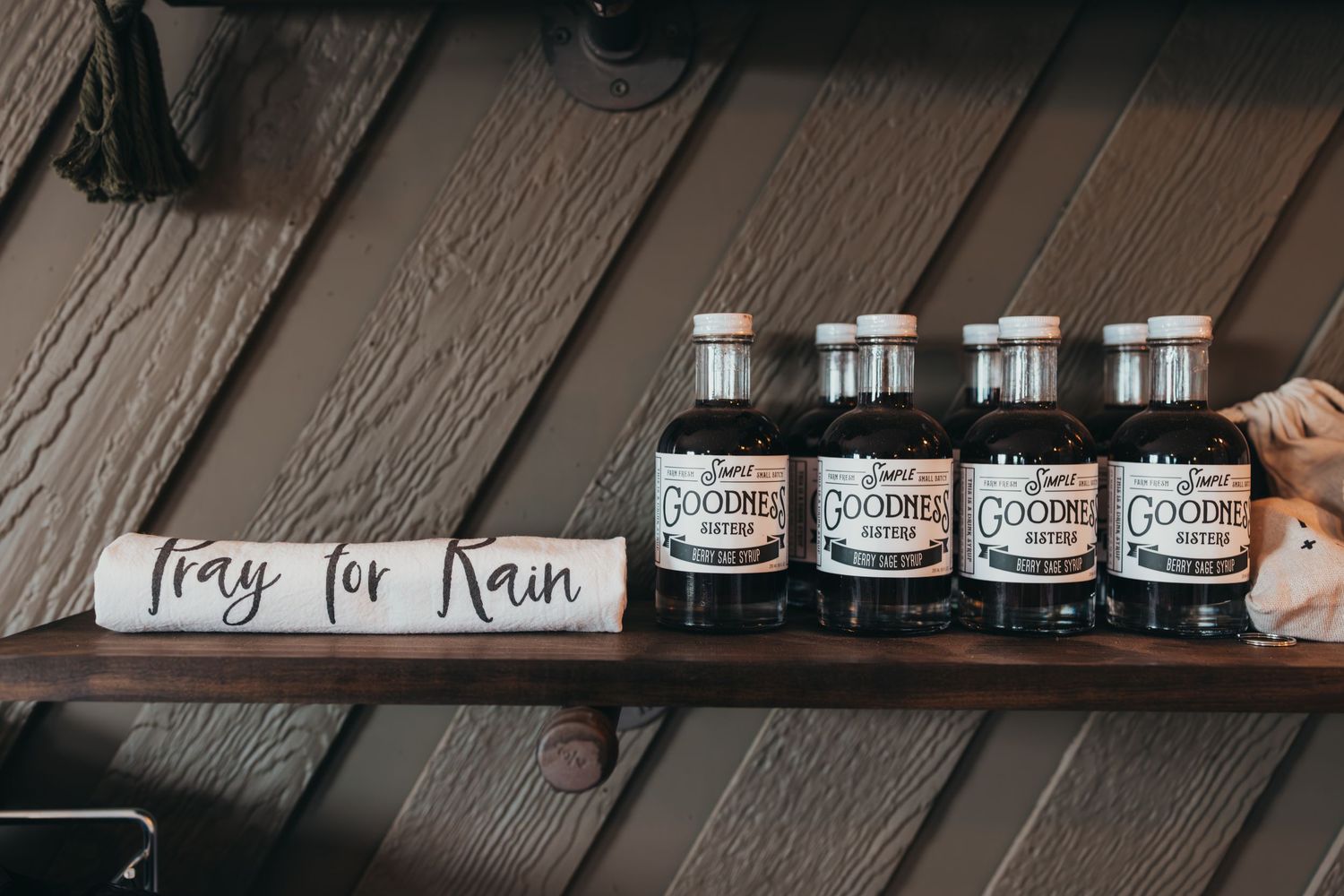 A wooden serving tray with four black glass bottles labeled with vintage-style apothecary tags sits on a dark surface.
