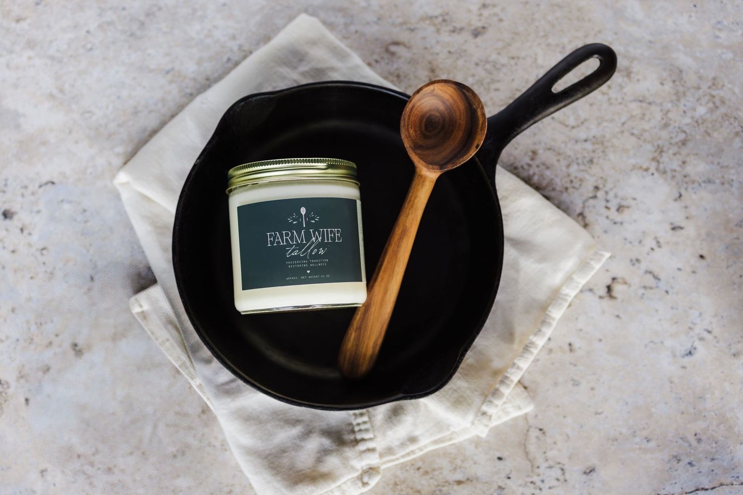 A glass jar filled with white cream on a black cast iron pan with a wooden spoon on marble surface.