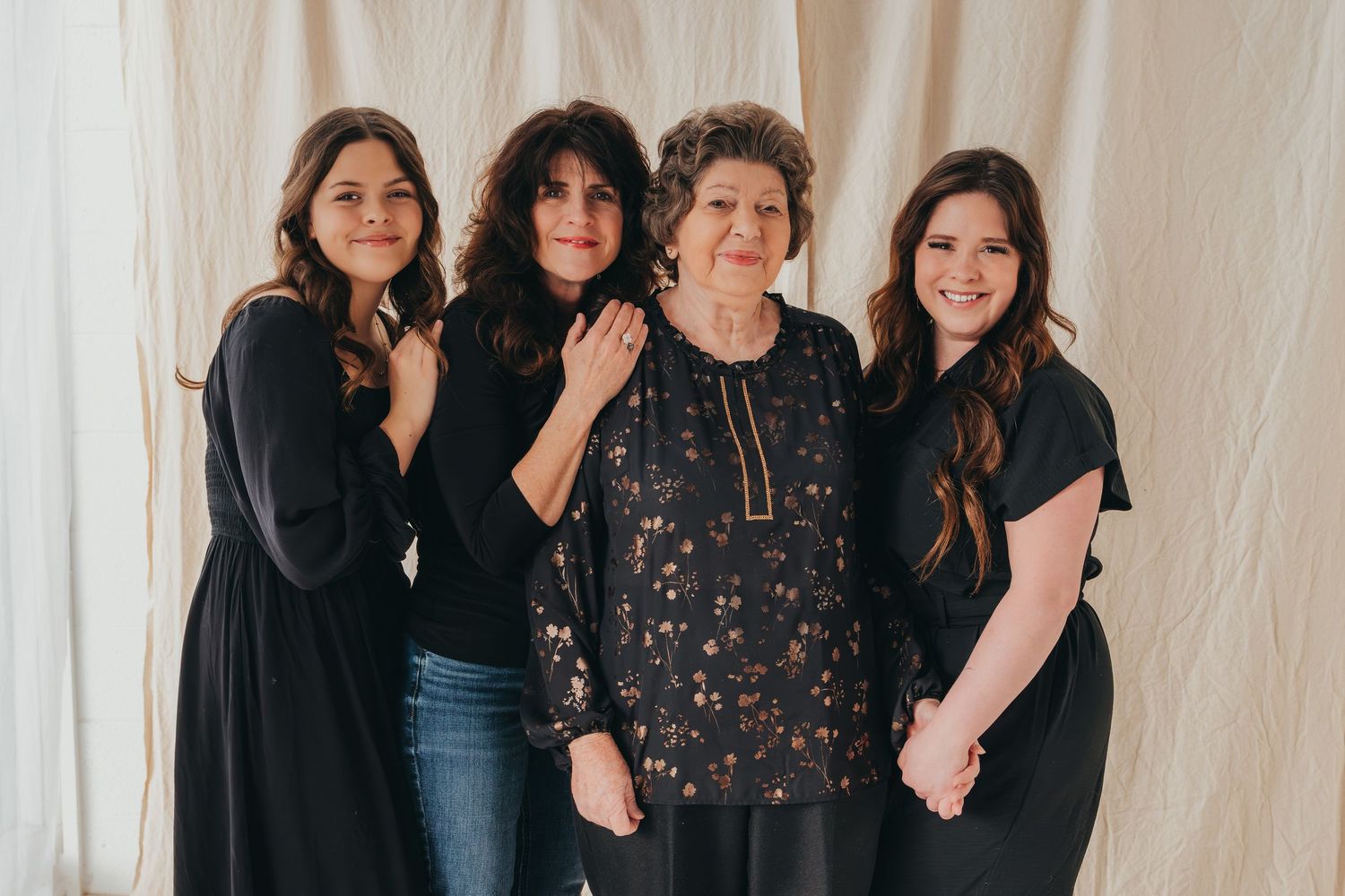 Four women in dark clothing posing against white backdrop.