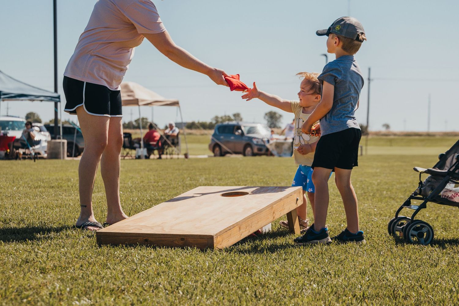 People enjoy playing cornhole game outdoors on a sunny day as they compete on grass field with wooden boards.