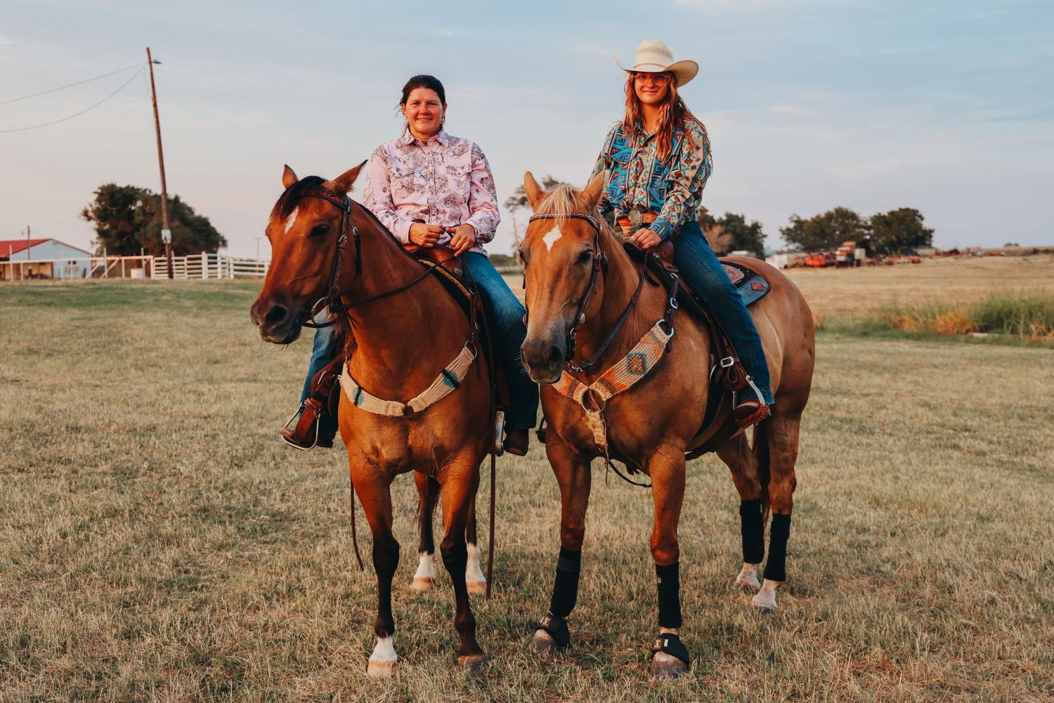 Two riders on brown horses pose together in an open field at sunset.