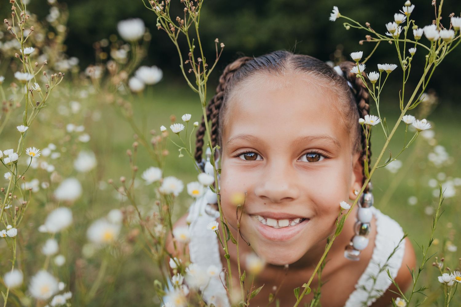 Someone smiles joyfully while surrounded by delicate white wildflowers in a sunny meadow.