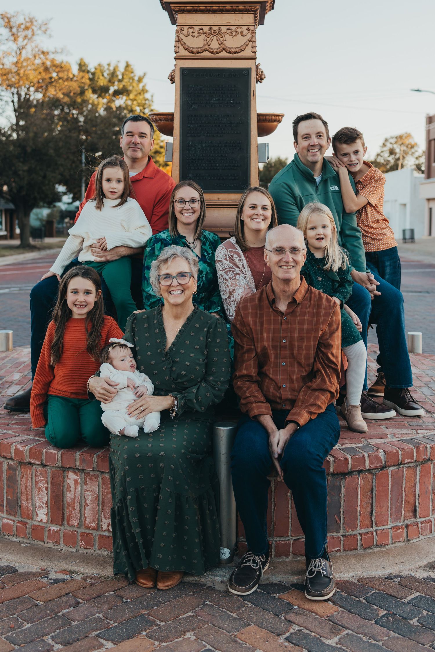 Multi-generational family portrait gathered around a brick monument outdoors during a fall holiday photo session.