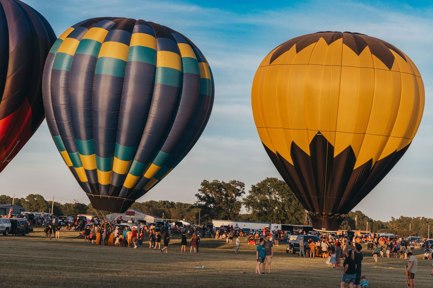 Two hot air balloons, one blue striped and one orange, stand inflated against blue sky.