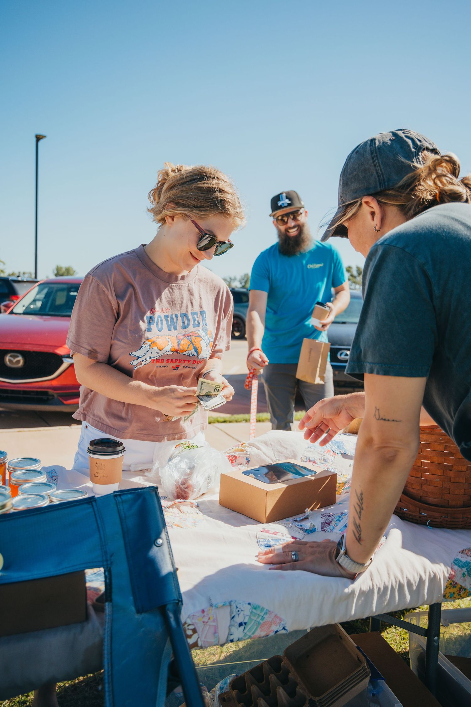 People working together at white tables during an outdoor craft or activity event.