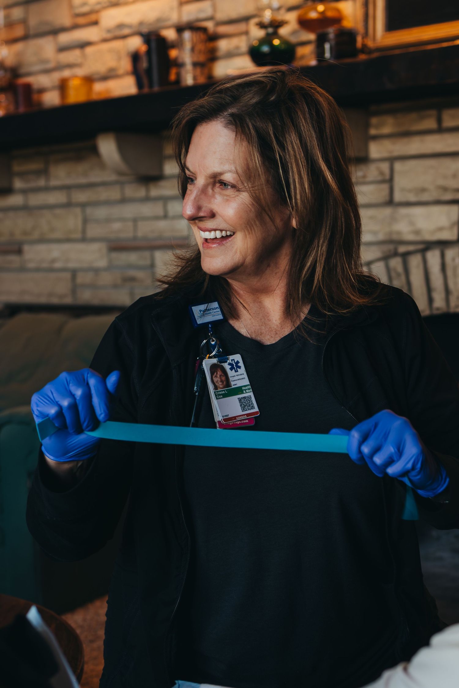 Smiling female healthcare worker in blue gloves stretches a resistance band during a therapy session.