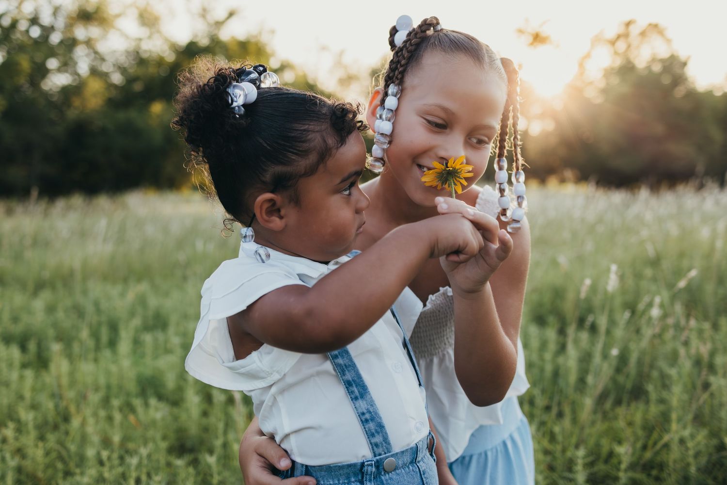 Children in denim overalls play and embrace in a golden sunlit field during sunset.